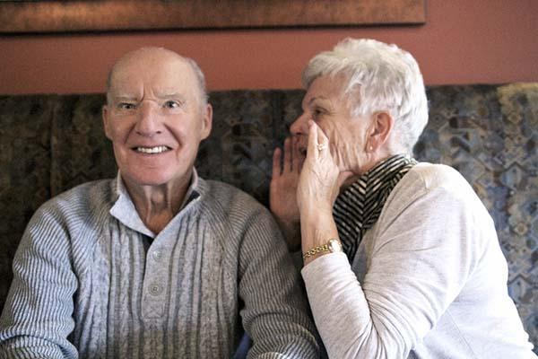 A senior woman shouts a few inches from her husband's ear; the concept is hearing loss.