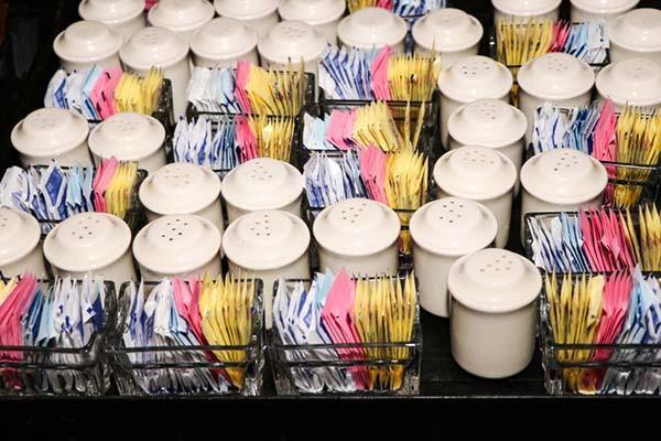Close-up of restaurant food-service trays with packets of artificial sweeteners and salt and pepper shakers.