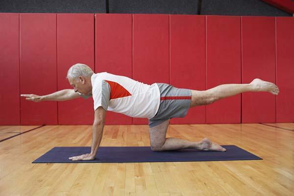 A senior man performs the bird dog exercise on a mat.