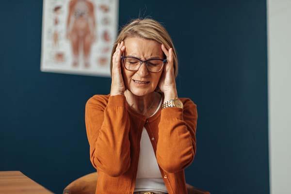 A middle-age woman grimaces and holds her hands to her temples as she experiences headache pain.