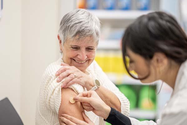 A smiling senior woman holds up her sleeve as a nurse applies a bandage to her arm after giving her a vaccination.