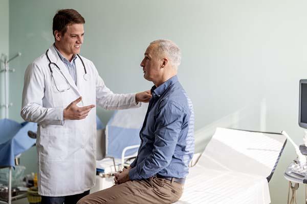 A doctor talks with a middle-age man in an exam room.