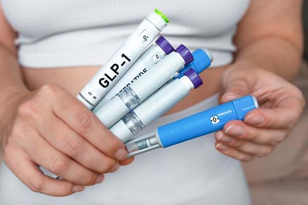 Close-up of the hands of a woman holding several injection pens containing GLP-1 medications.