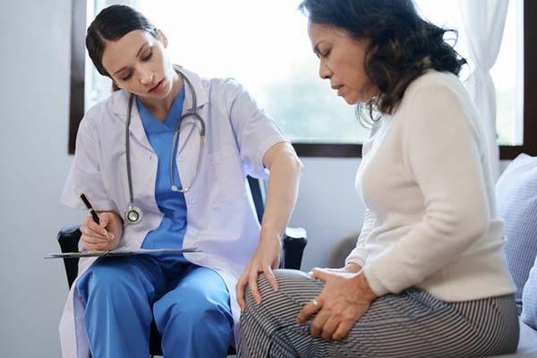 A female doctor examines the knee of a woman who appears to be in pain.