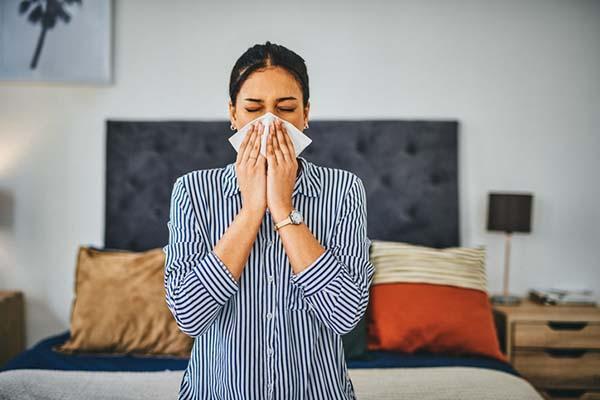 A woman holds a tissue to her face as she blows her nose.