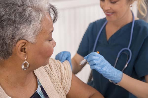 A nurse holding a syringe is about to give a vaccination to a senior woman.
