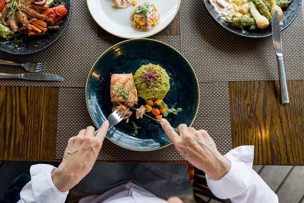 Overhead view of a person cutting into a piece of salmon on a black plate, served with rice and vegetables.