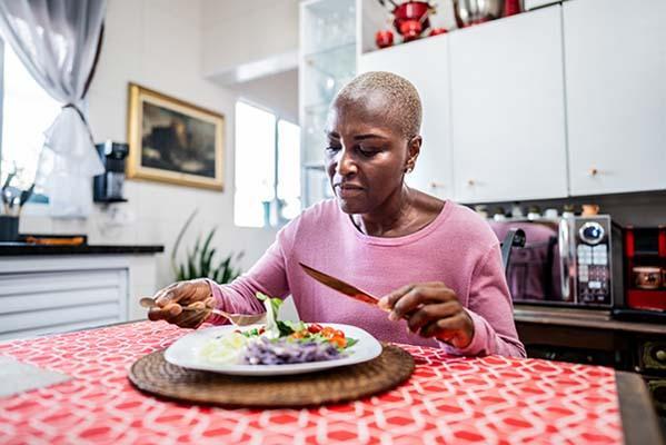 A mature woman eats a salad while sitting at a table in her kitchen.