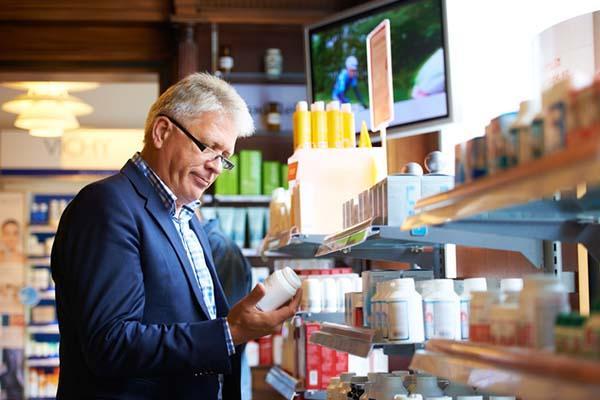 A mature man in a drug store reads the label on a bottle.