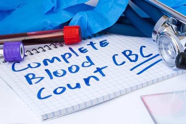 The words complete blood count (CBC) are written on a pad laid next to tubes of blood for testing, protective gloves, and a stethoscope.