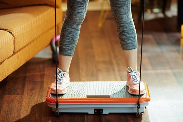 The legs and feet of a woman exercising at home using a vibration plate.