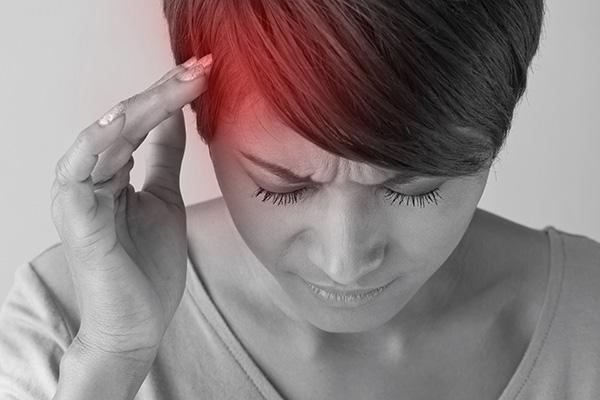 Black and white close-up of a woman experiencing headache pain, represented by a red tint centered on one side of her forehead.