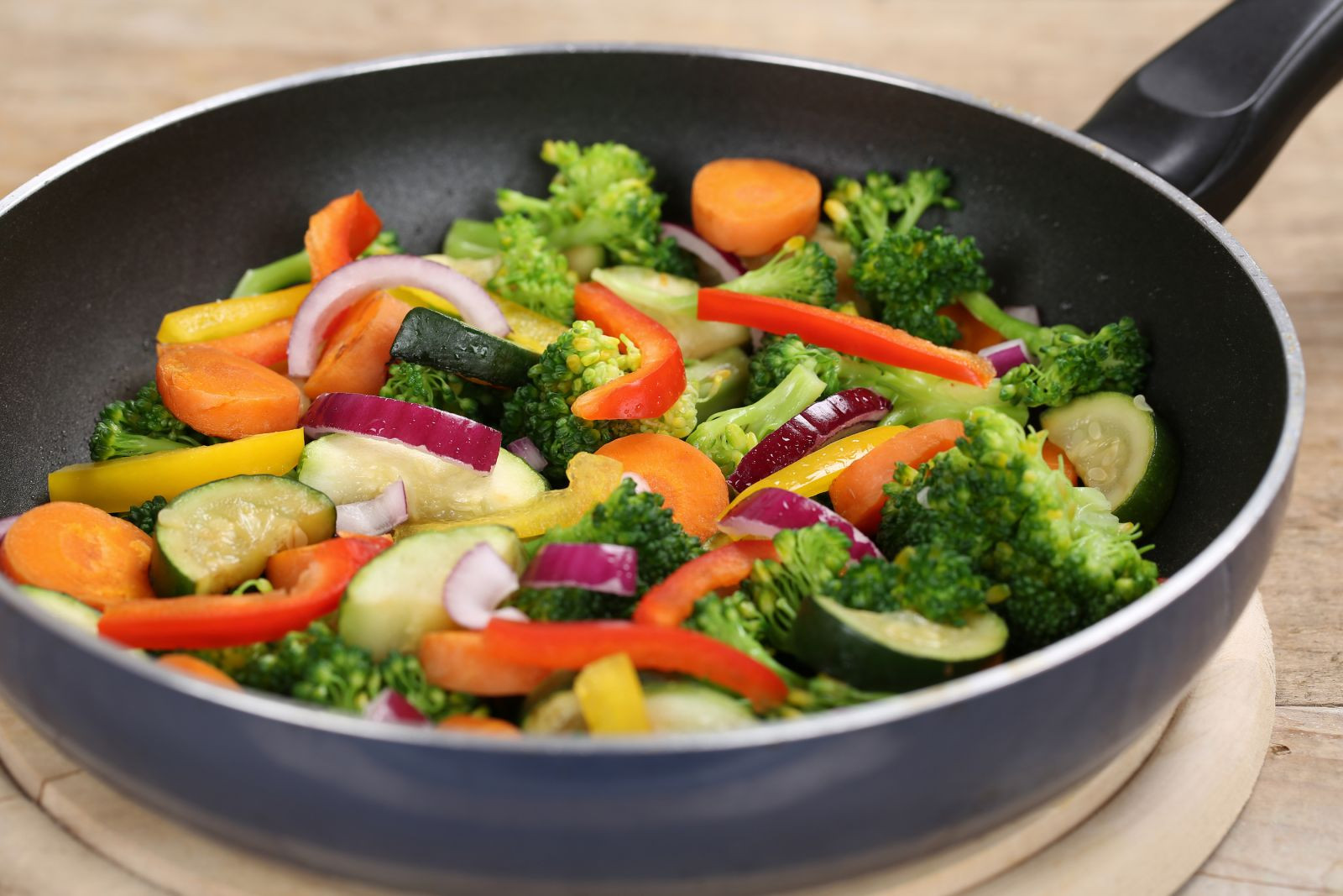  A variety of vegetables, including broccoli, carrots, bell peppers, and zucchini, are being cooked in a frying pan.