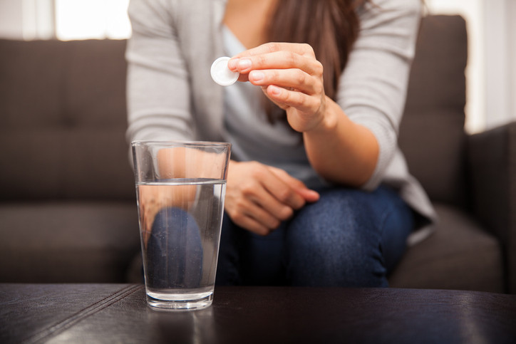 Closeup of a young brunette sitting on a couch about to take an effervescent antacid.