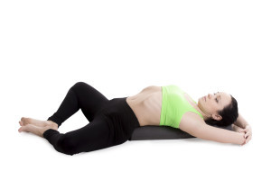 Sporty girl on white background resting in Reclining Bound Angle yoga Pose, Supta Baddha Konasana, restorative, relaxing asana, using bolster
